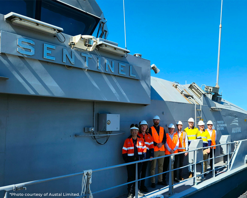 work men standing next to a large sea vessel called The Sentinel